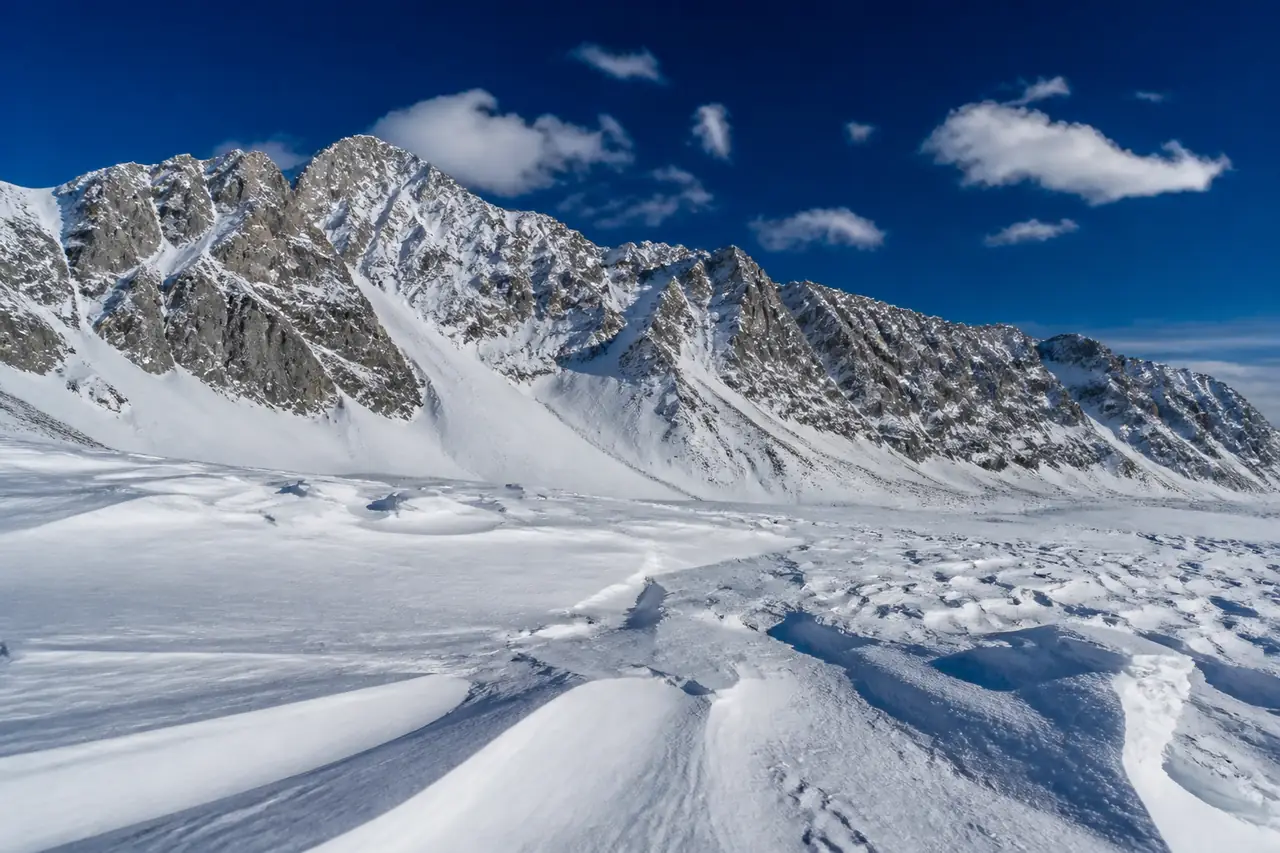 Altopiano calcareo innevato senza vegetazione, con neve modellata dal vento e una lunga cresta rocciosa sullo sfondo
