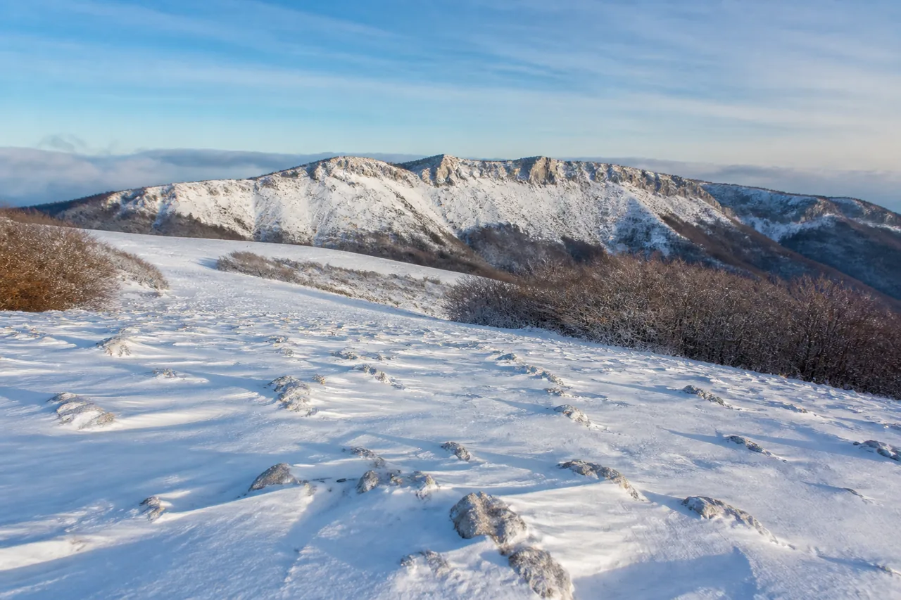 Altopiano calcareo innevato con neve modellata dal vento e una lunga cresta sul fondo