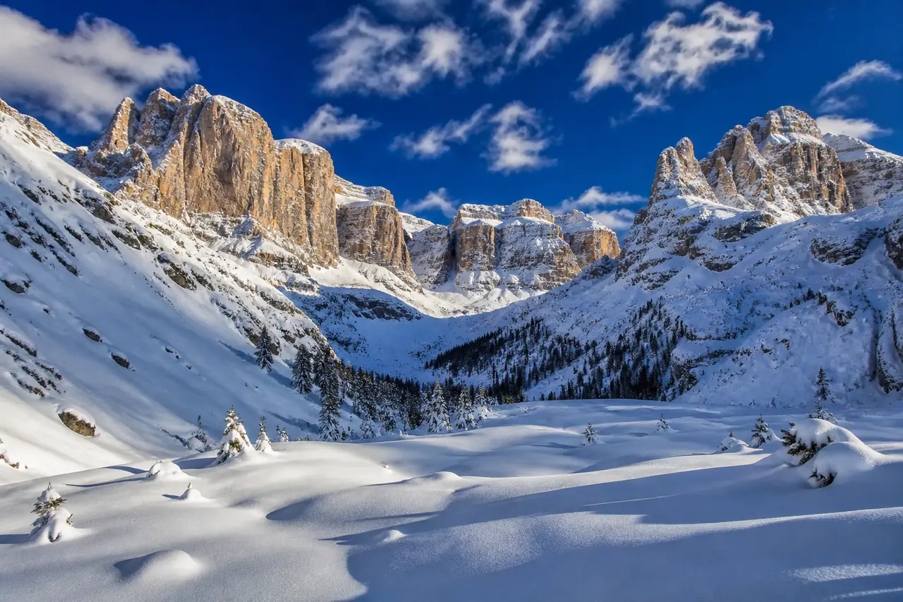 Anfiteatro di pareti dolomitiche che chiude una valle innevata, con boschi di conifere sul fondo